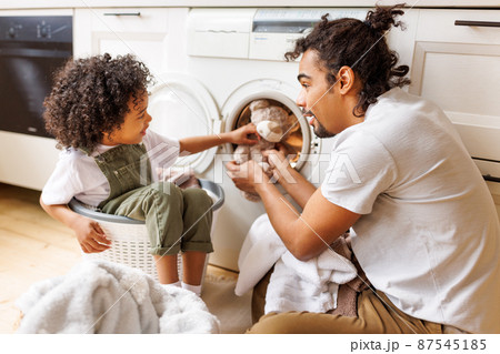 Son helping dad to load washing machine Son helping dad to load washing machine 87545185