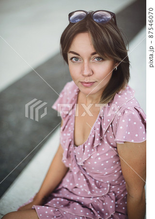 Portrait of a young beautiful brunette posing on the street in a soft pink sundress Portrait of a young beautiful brunette posing on the street in a soft pink sundress 87546070