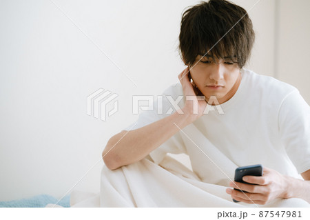 ベッドでスマホを見る若い男性 87547981