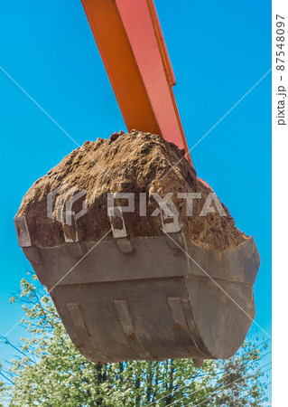 Excavation works. Tractor bucket digging the ground on a construction site against the sky Excavation works. Tractor bucket digging the ground on a construction site against the sky 87548097