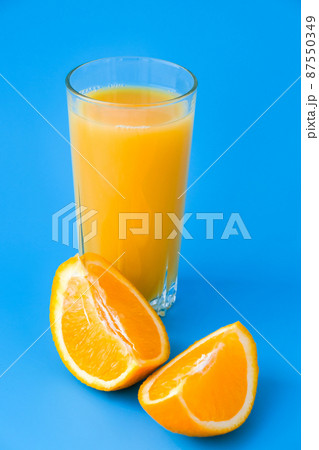 Glass bottle of fresh squeezing Orange juice with sliced fruits on blue background. Fruit juice, fresh cold drink. Refreshment in summer. Fruits cut in half Glass bottle of fresh squeezing Orange juice with sliced fruits on blue background. Fruit juice, fresh cold drink. Refreshment in summer. Fruits cut in half 87550349