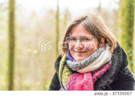 Portrait of a thirty year old white woman with a colorful scarf, glasses and a green bokeh nature background Portrait of a thirty year old white woman with a colorful scarf, glasses and a green bokeh nature background 87550567