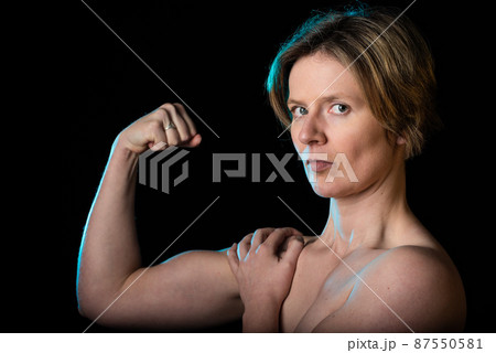 Low key studio portrait of a 35 year old white woman with naked shoulders showing her biceps 87550581