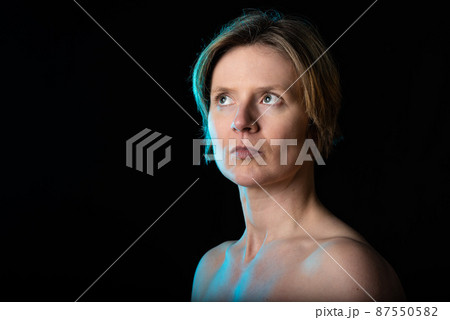Low key studio portrait of a 35 year old white woman with naked shoulders showing her biceps 87550582