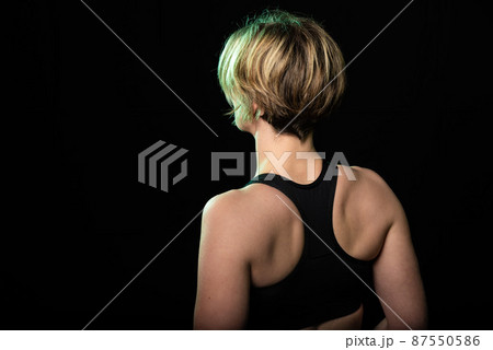 Low key studio portrait of a 35 year old white woman showing her back in a fitness top 87550586