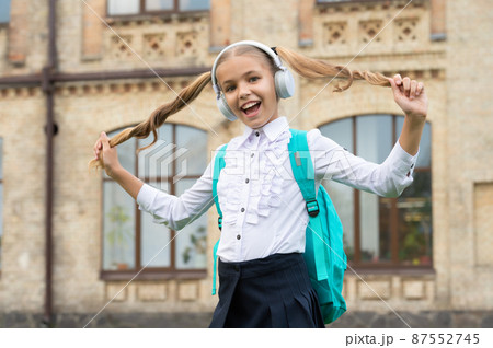 Happy school girl in uniform having fun listening to music in headphones and holding hair 87552745