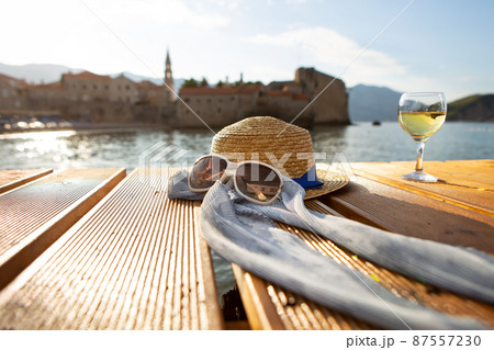 A straw hat, glasses and a glass of wine stands on a pier near the sea, close-up. Beautiful light from the sun. Place for text. A straw hat, glasses and a glass of wine stands on a pier near the sea, close-up. Beautiful light from the sun. Place for text. 87557230