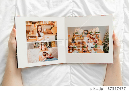 a hands holds a book with photos of mom, dad and daughter in the photo studio. a hands holds a book with photos of mom, dad and daughter in the photo studio. 87557477