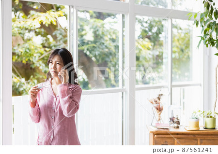 体温計の検温結果を見てどこかに電話をかけるパジャマの女性 体温計の検温結果を見てどこかに電話をかけるパジャマの女性 87561241