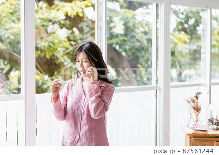 体温計の検温結果を見てどこかに電話をかけるパジャマの女性 体温計の検温結果を見てどこかに電話をかけるパジャマの女性 87561244