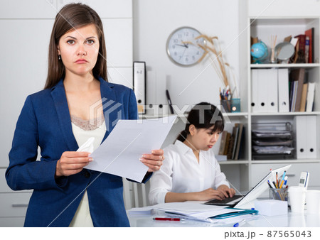 Business woman crying standing in office with working colleague behind Business woman crying standing in office with working colleague behind 87565043