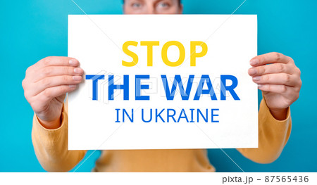 Young woman cover half face banner with Stop the war in Ukraine inscription isolated over blue color background Young woman cover half face banner with Stop the war in Ukraine inscription isolated over blue color background 87565436