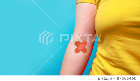 Blood donation. Blood donor woman in yellow T-shirt with patch bandage after giving blood on a blue background. World blood donor day and save life concept. Blood donation. Blood donor woman in yellow T-shirt with patch bandage after giving blood on a blue background. World blood donor day and save life concept. 87565460