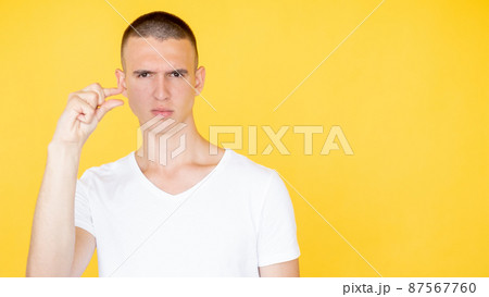 Small size. Serious man. Measurement gesture. Concentrated handsome guy showing fingers sign of little bit isolated yellow copy space. 87567760