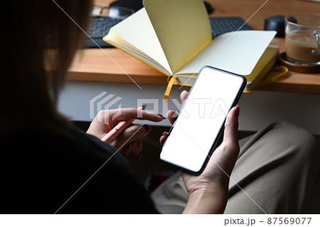 Over shoulder view woman sitting and her workplace and using smart phone. 87569077