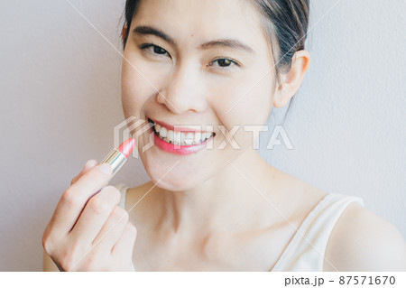 Portrait of happiness Asian woman holding a lipstick and applying to her lips. Conceptual of beauty and cosmetics shot. Portrait of happiness Asian woman holding a lipstick and applying to her lips. Conceptual of beauty and cosmetics shot. 87571670