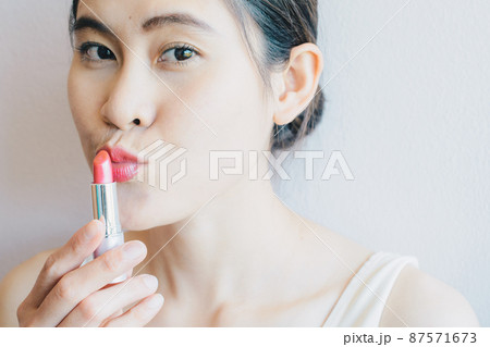 Portrait of Asian woman holding a lipstick and applying her lips. Conceptual of beauty and cosmetics shot. 87571673