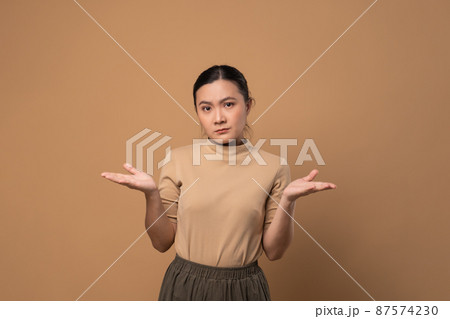 Asian woman feel confuse, standing isolated on beige background. Asian woman feel confuse, standing isolated on beige background. 87574230