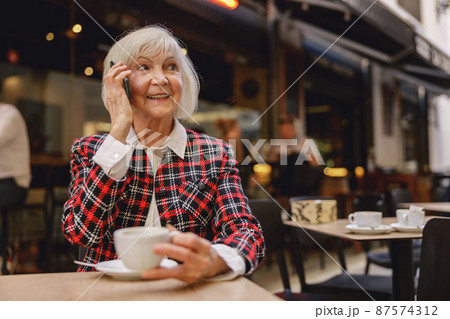 Positive pensioner female having coffee at cafe 87574312