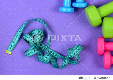 Dumbbells and measure tape in cyan color on purple texture 87580627