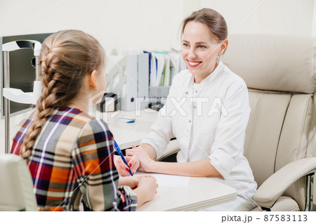 doctor interviews little girl before being examined in ophthalmologist's office. 87583113