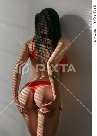 Young brunette woman in red lingerie posing in a sunshine Young brunette woman in red lingerie posing in a sunshine 87584039