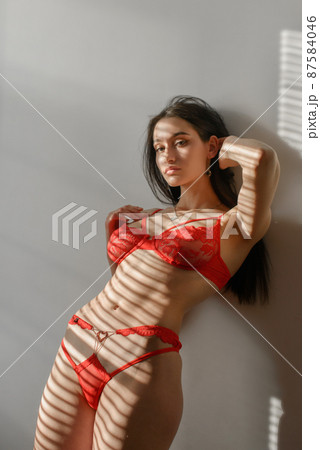 Young brunette woman in red lingerie posing in a sunshine Young brunette woman in red lingerie posing in a sunshine 87584046
