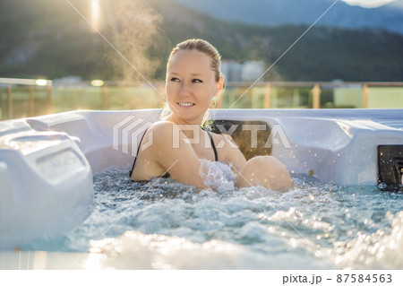 Portrait of young carefree happy smiling woman relaxing at hot tub during enjoying happy traveling moment vacation life against the background of green big mountains Portrait of young carefree happy smiling woman relaxing at hot tub during enjoying happy traveling moment vacation life against the background of green big mountains 87584563