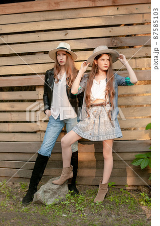 Two teenage girls wearing country style clothes standing against wooden planks wall background Two teenage girls wearing country style clothes standing against wooden planks wall background 87585103
