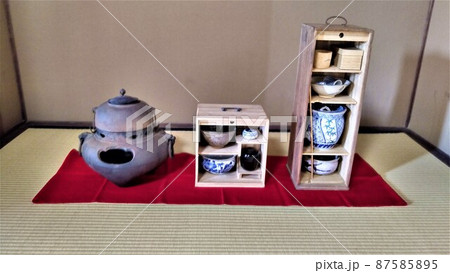 茶道、お茶の道具、畳に緋毛氈を敷いて茶釜、木の箱に入った抹茶茶碗、棗、茶杓、建水等が置かれている 87585895
