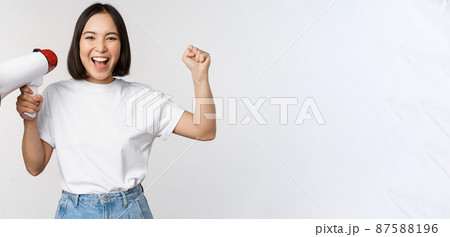 Happy asian woman shouting at megaphone, making announcement, advertising something, standing over white background 87588196