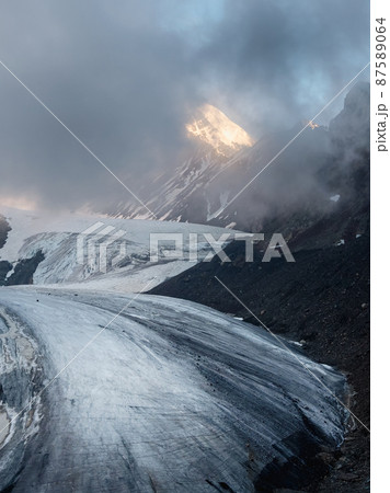 Twilight Mountains. Light on the glacier. Majestic glacier is illuminated by the bright golden evening sun. Vertical view. Big Aktru Glacier, Altai Mountains. Twilight Mountains. Light on the glacier. Majestic glacier is illuminated by the bright golden evening sun. Vertical view. Big Aktru Glacier, Altai Mountains. 87589064