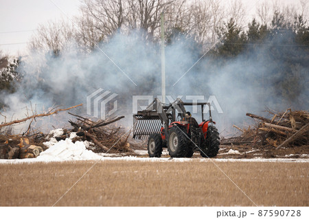 Tractor Moves Brush During a Controlled Burn on a Farm Property to Increase Arable Land Tractor Moves Brush During a Controlled Burn on a Farm Property to Increase Arable Land 87590728