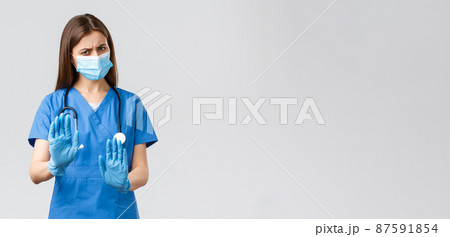 Covid-19, preventing virus, health, healthcare workers concept. No thank you. Displeased and reluctant female nurse or doctor in medical mask and scrubs, make stop, rejection or refusal sign 87591854