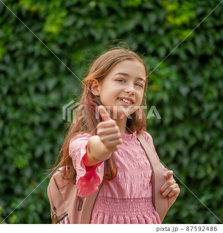 The girl shows like gestures. Teen girl in a pink dress with a backpack. 87592486