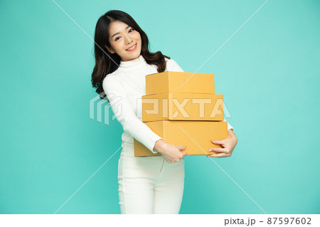 Happy Asian woman smiling and holding package parcel box isolated on green background, Delivery courier and shipping service concept 87597602