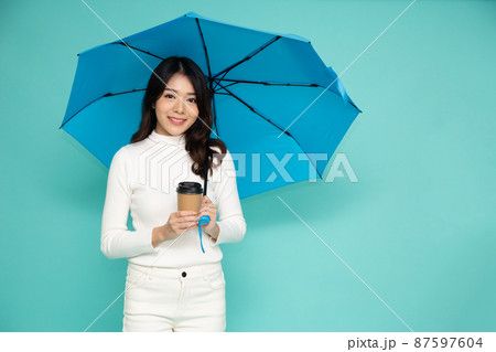 Young happy Asian woman holding blue umbrella and hot coffee cup isolated on green background 87597604