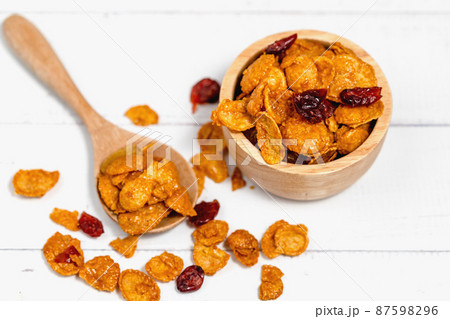 The wooden bowl of caramel cornflakes with raisins on white background 87598296