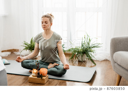 Beautiful happy girl with closed eyes practicing yoga in lotus position in bedroom in the morning 87603850