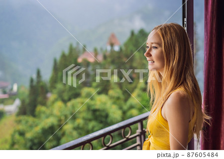 A young woman holding coffee cup while sittinhg on chair on balcony , looking at mountains and green nature. Woman in Sapa in the fog, Northwest Vietnam. Vietnam travel concept. UNESCO heritage A young woman holding coffee cup while sittinhg on chair on balcony , looking at mountains and green nature. Woman in Sapa in the fog, Northwest Vietnam. Vietnam travel concept. UNESCO heritage 87605484