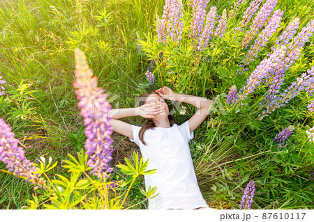 Happy teenage girl smiling outdoor. Beautiful young teen woman resting lying on summer field with blooming wild flowers green background. Free happy kid relaxing and enjoying nature Happy teenage girl smiling outdoor. Beautiful young teen woman resting lying on summer field with blooming wild flowers green background. Free happy kid relaxing and enjoying nature 87610117
