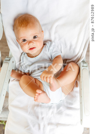 Cute little newborn girl with smiling face looking at camera on white background. Infant baby resting playing lying down on feeding chair at home. Motherhood happy child concept 87612989