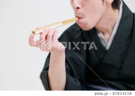 扇子を使ってタバコを吸うモノマネをする落語家 87614218