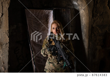 Caucasian woman in army uniform holding a machine gun and standing near an open coffin.  87614383