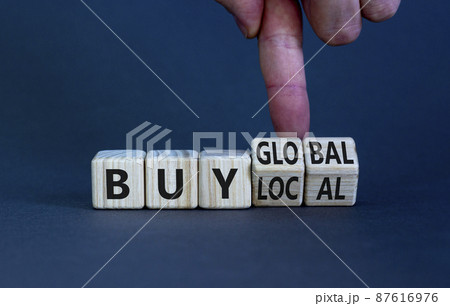 Buy local or global symbol. Businessman turns wooden cubes, changes words 'buy local' to 'buy global'. Beautiful grey table, grey background. Business, buy local or global concept. Copy space. 87616976