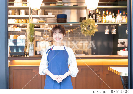 カフェでお出迎えをするエプロンをした若い女性店員 カフェでお出迎えをするエプロンをした若い女性店員 87619480