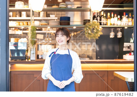 カフェでお出迎えをするエプロンをした若い女性店員 87619482