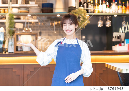カフェでお出迎えをするエプロンをした若い女性店員 カフェでお出迎えをするエプロンをした若い女性店員 87619484