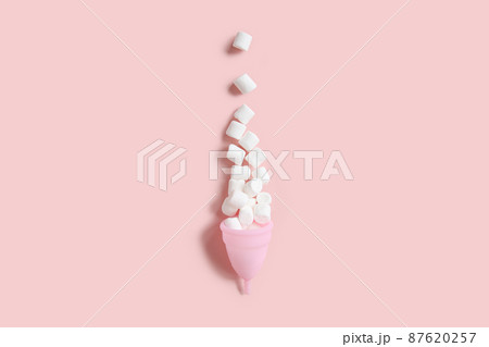 Pink menstrual cup and white mini marshmallow like blood drop with shadow on pink background. Women's health, alternative hygiene and ecology of planet. Top front view, copy space, flat lay. 87620257