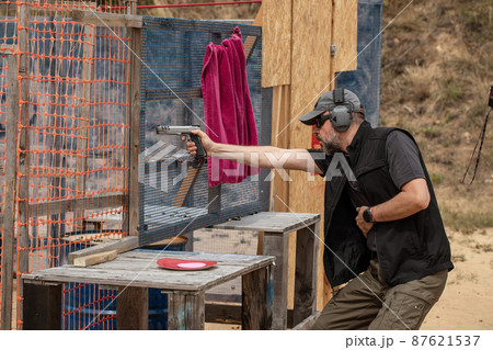Man in tactical clothes shooting from a pistol, reloading the gun and aiming at the target in the opendoor Shooting range 87621537
